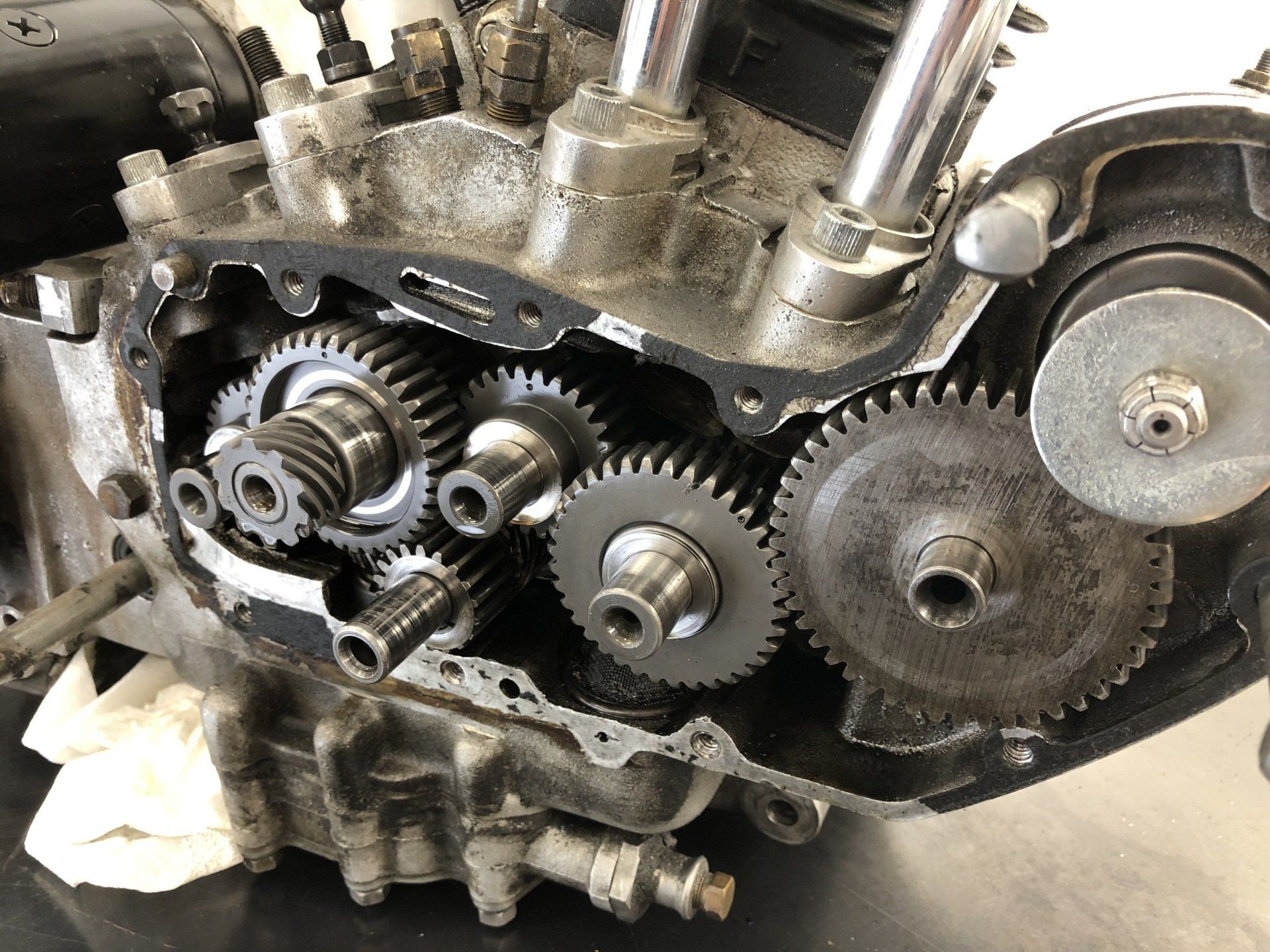Exposed engine timing gears and chain inside a black metal housing, with bolts and mechanical parts visible.