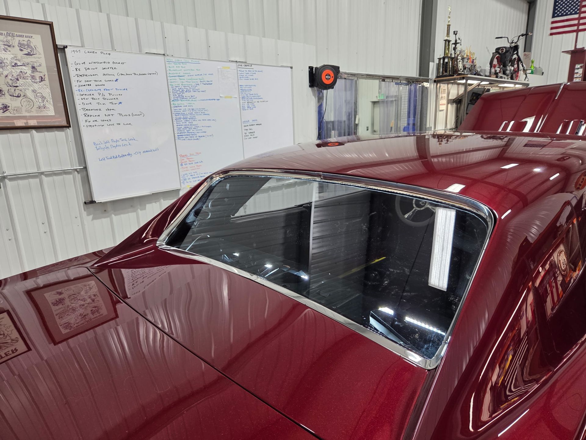 Red classic car in a garage, with a whiteboard wall and tools in the background