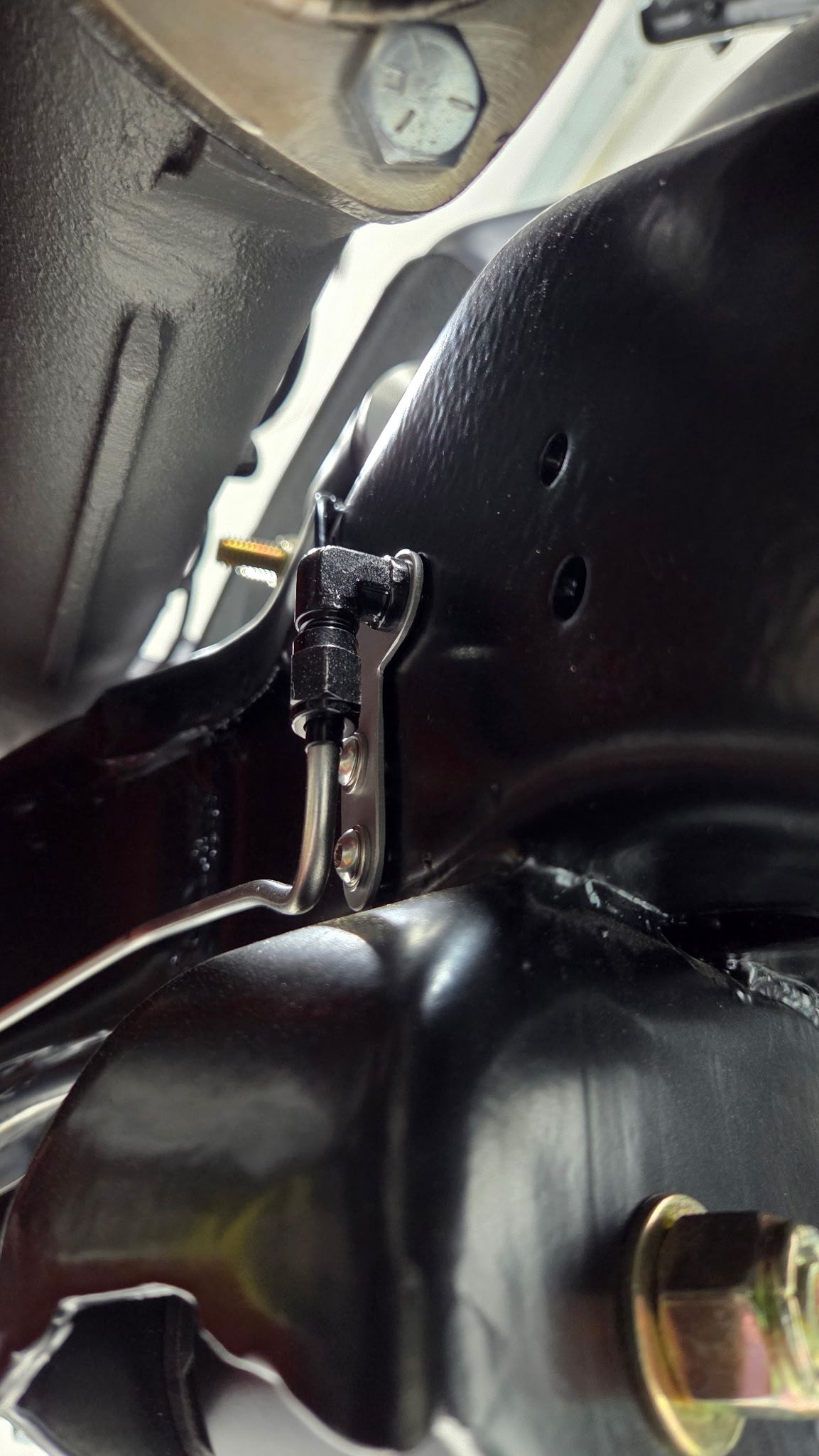 Close-up of a black metal hinge or bracket inside a vehicle interior, with bolts and textured trim.