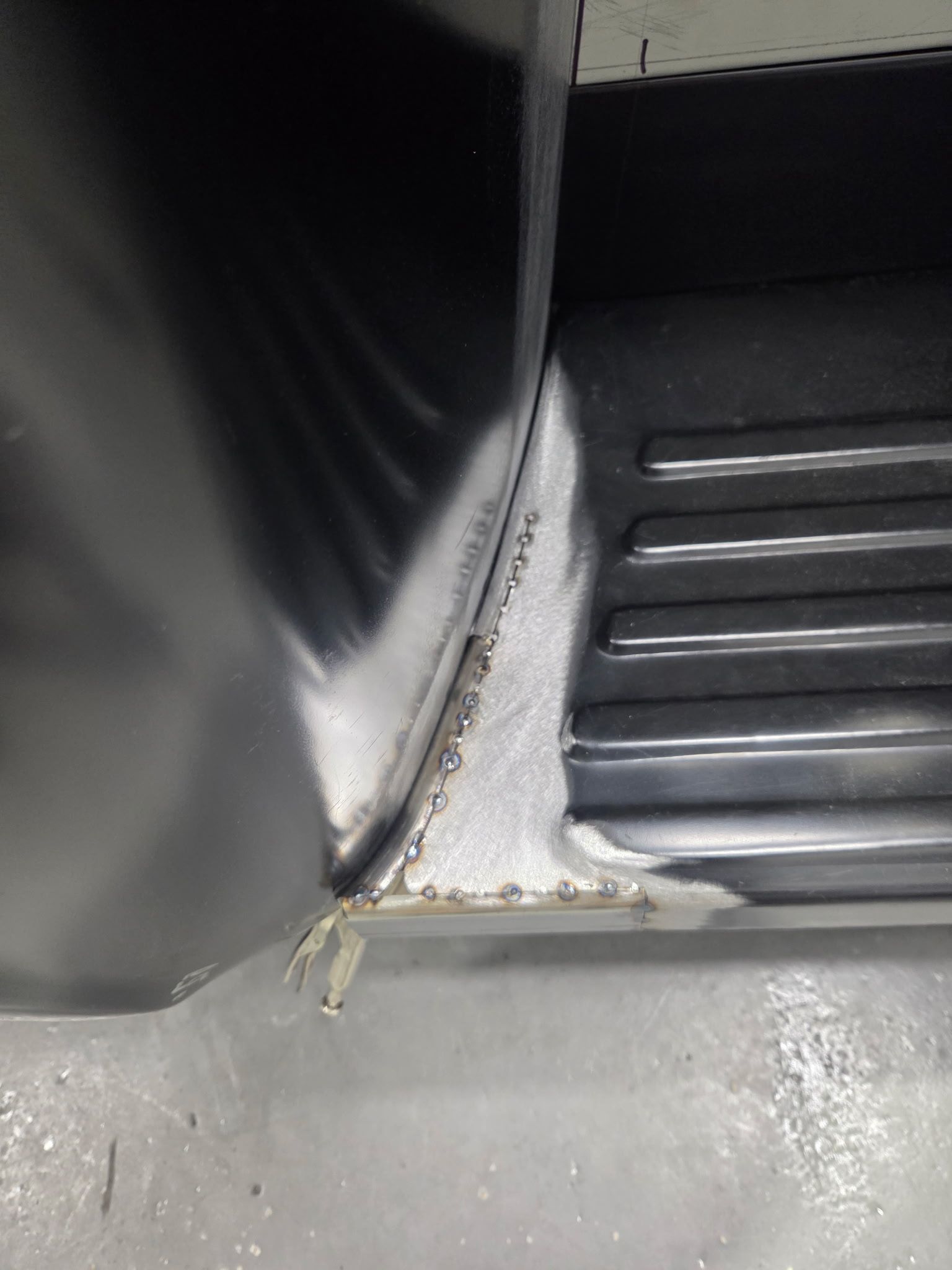 Close-up of a gray metal corner seam with white caulk and a black ribbed surface next to it.