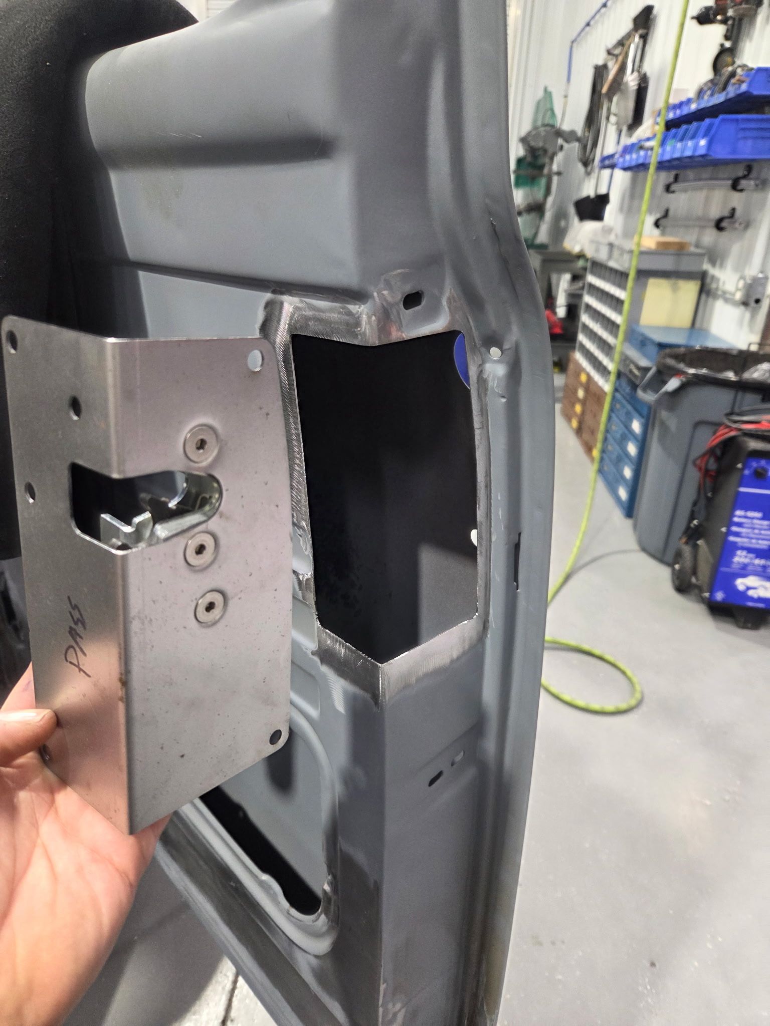 Close-up of a metal bracket being aligned with a cutout in a gray vehicle interior panel in a workshop.