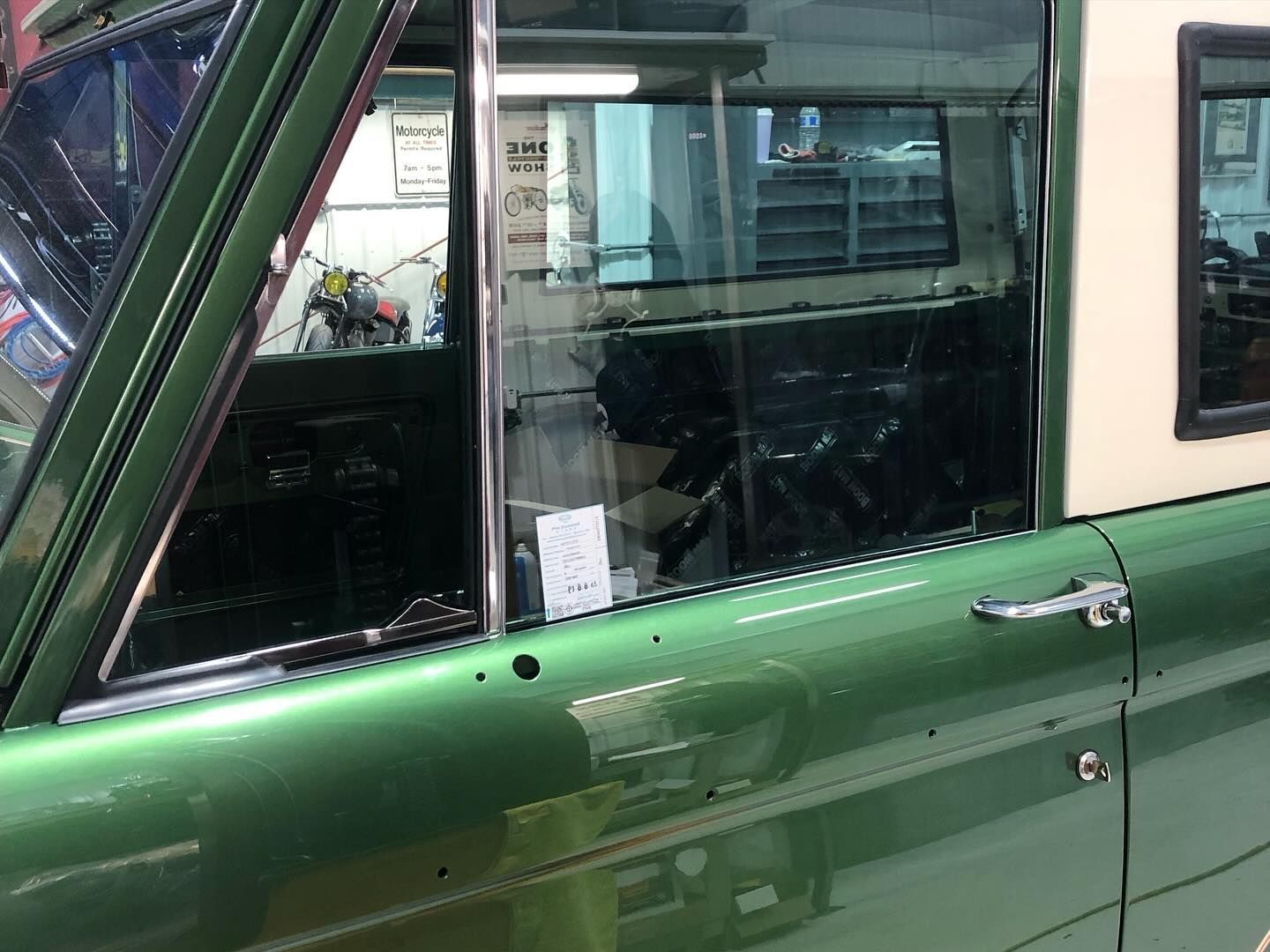 Green car door and window seen close up, with reflections on the glossy paint.