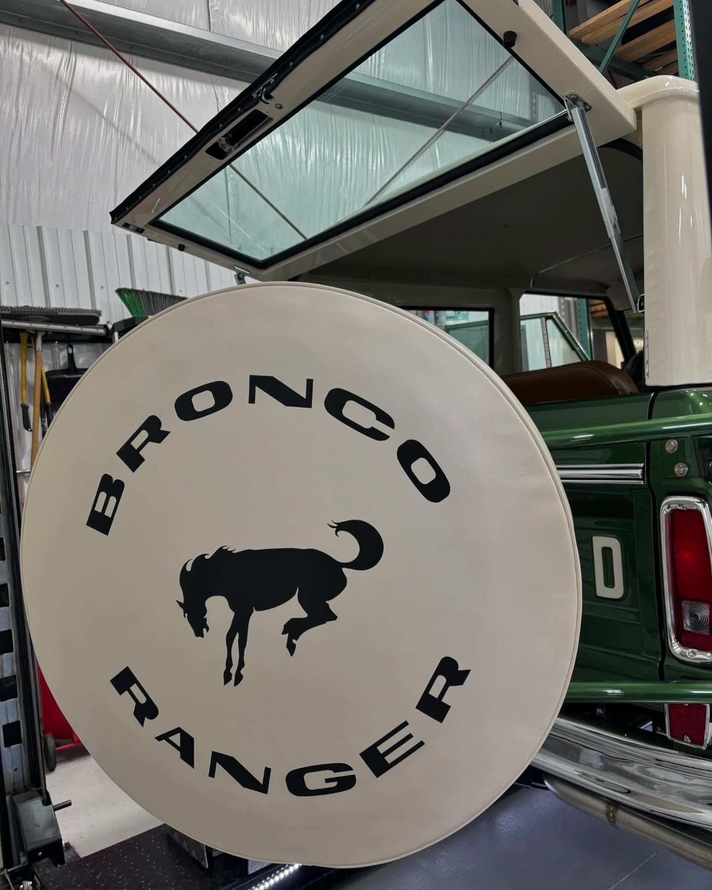 White Bronco Ranger spare tire cover with black bull logo on a green vehicle under a canopy