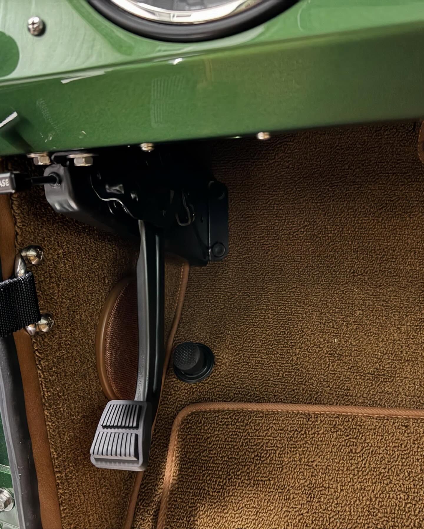 Car’s green dashboard and metal foot pedals above a brown carpeted floor.