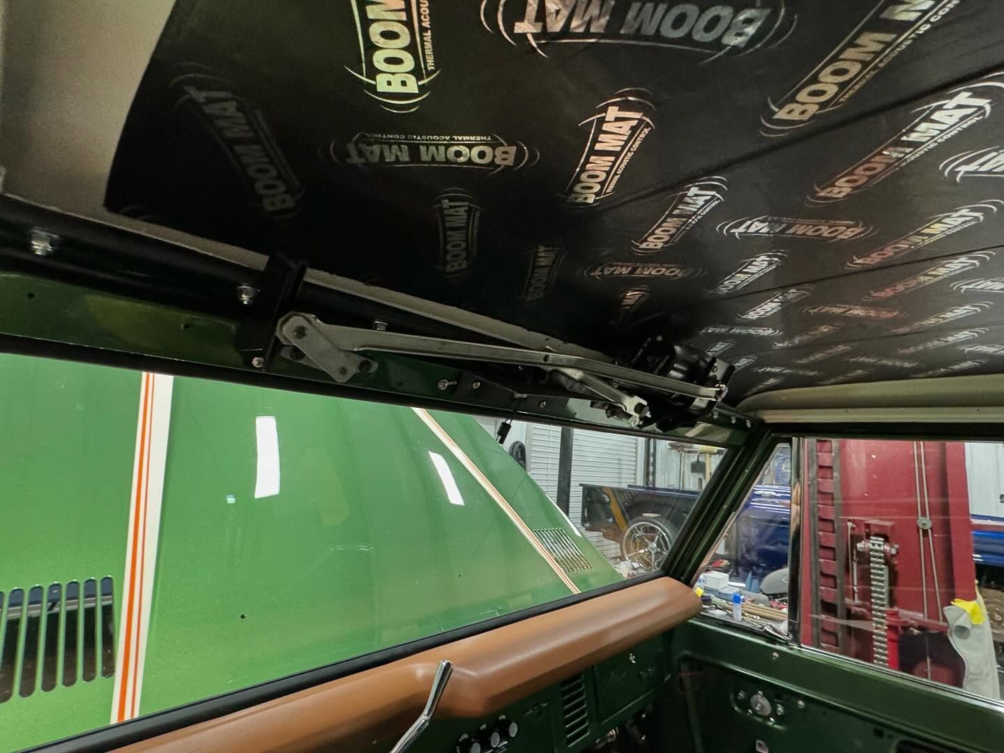 Interior of a race car with black headliner, wood dash, and green track visible through the windshield