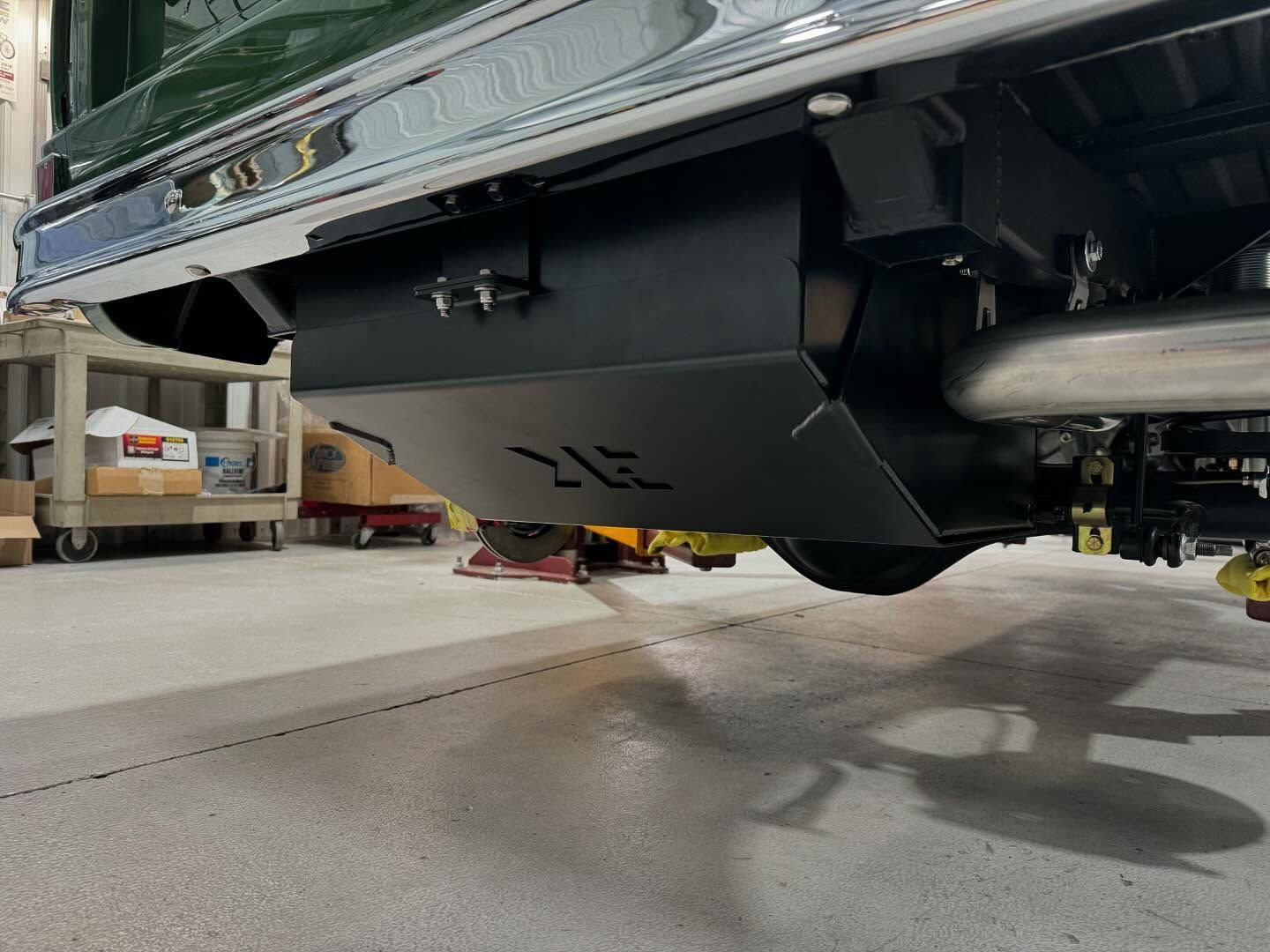 Black car lifted on a hoist in a garage, showing its undercarriage and rear axle.