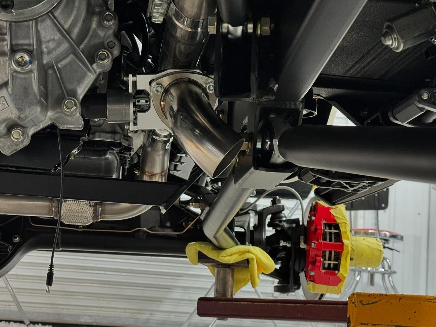 Undercarriage of a vehicle in a garage, with black exhaust piping and a red brake caliper visible.