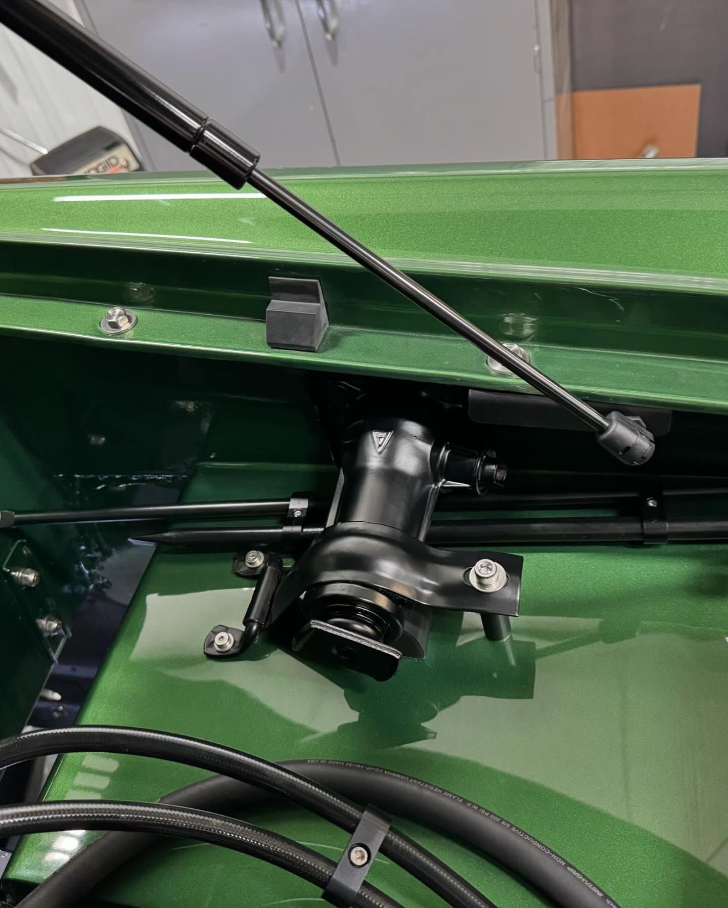 Green metal machinery compartment with black hydraulic cylinder and hoses, viewed close up