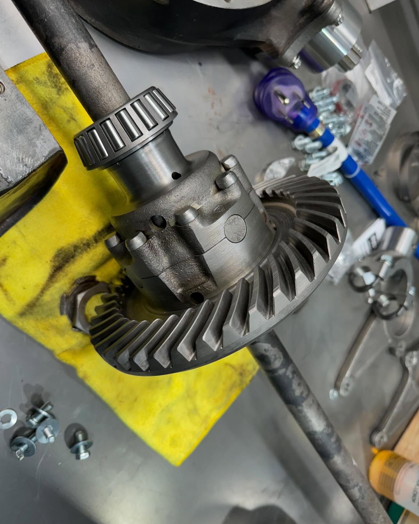 Metal differential gear assembly with ring gear on a workbench, surrounded by tools and bolts.