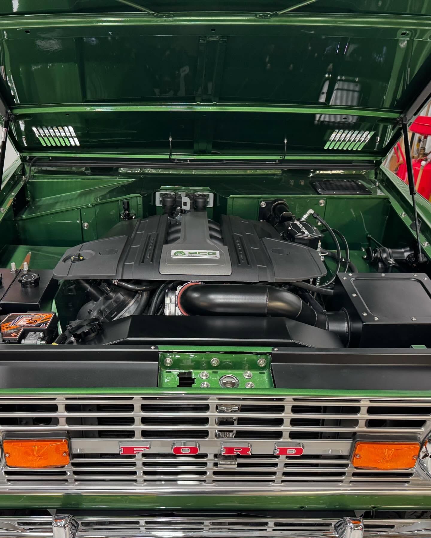 Open car hood showing a green engine bay with black engine components and chrome grille lights