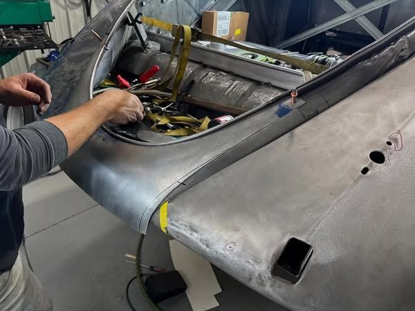 Worker repairing a gray aircraft fuselage with tools inside an open cockpit area