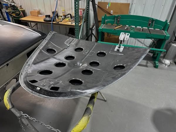 Large black metal car panel with circular cutouts resting on a workbench in a workshop.