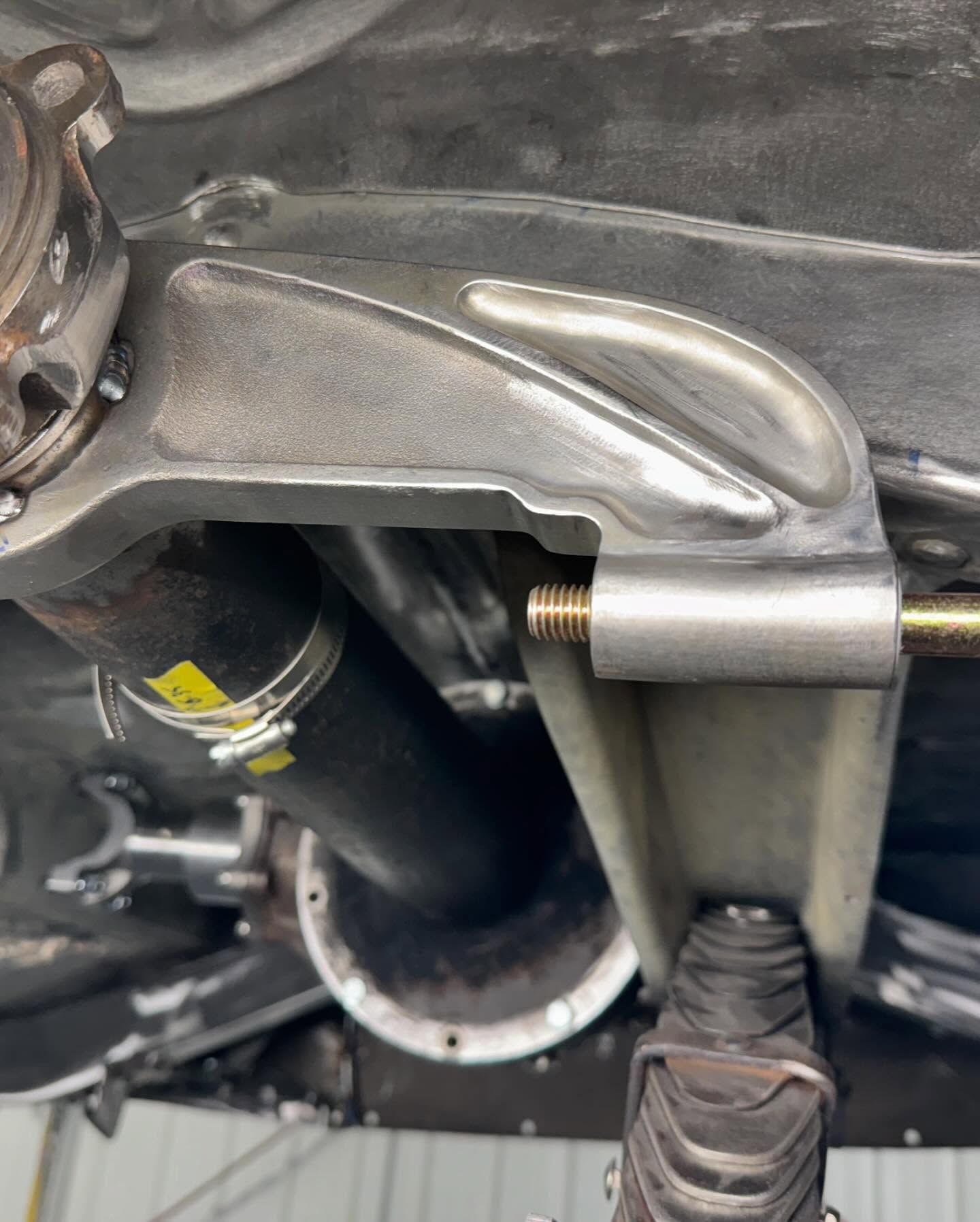 Close-up of a gloved hand using a metal tool on a vehicle undercarriage bolt near an exhaust pipe