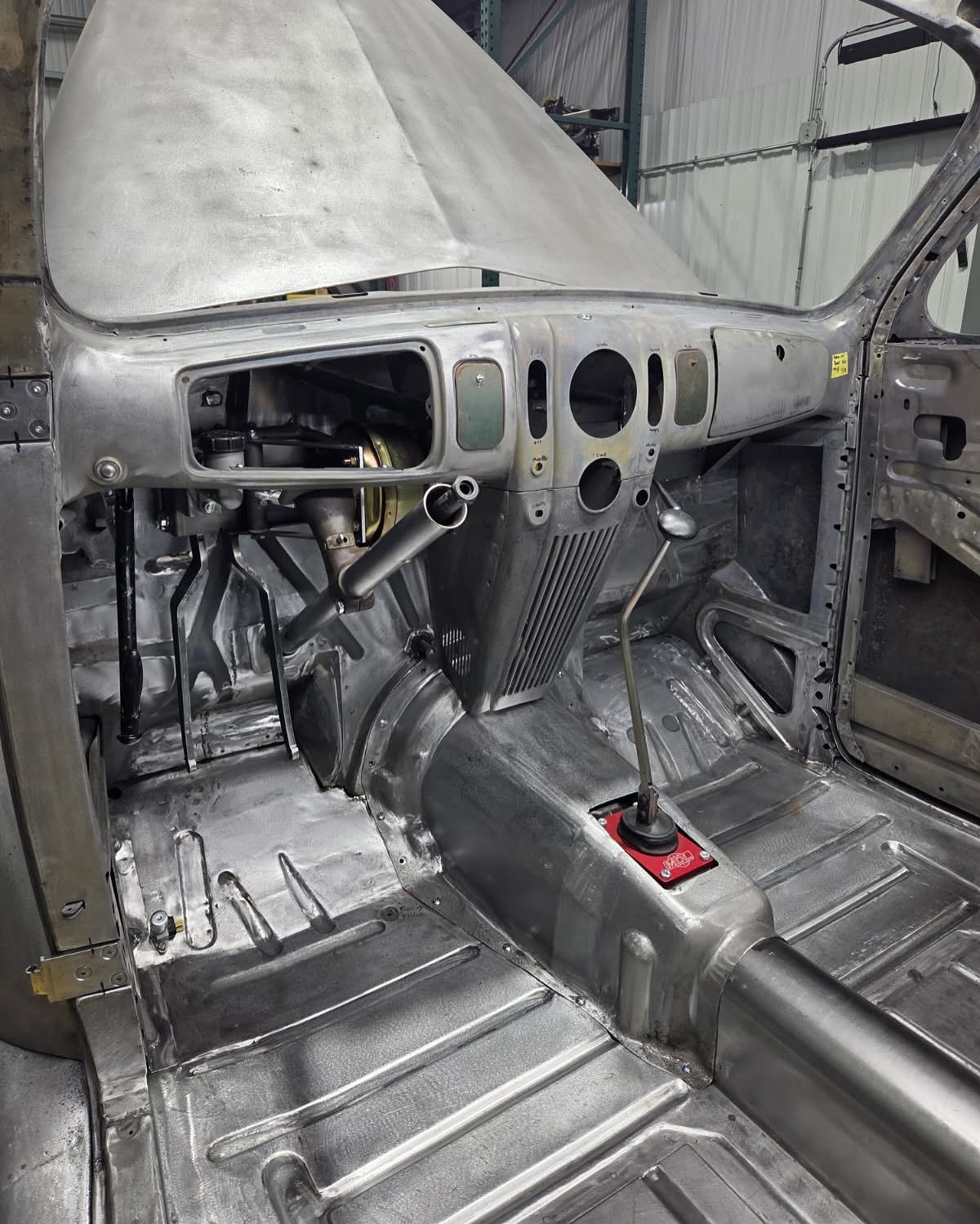 Exposed aircraft cockpit interior with bare metal panels, controls, and unfinished floor.