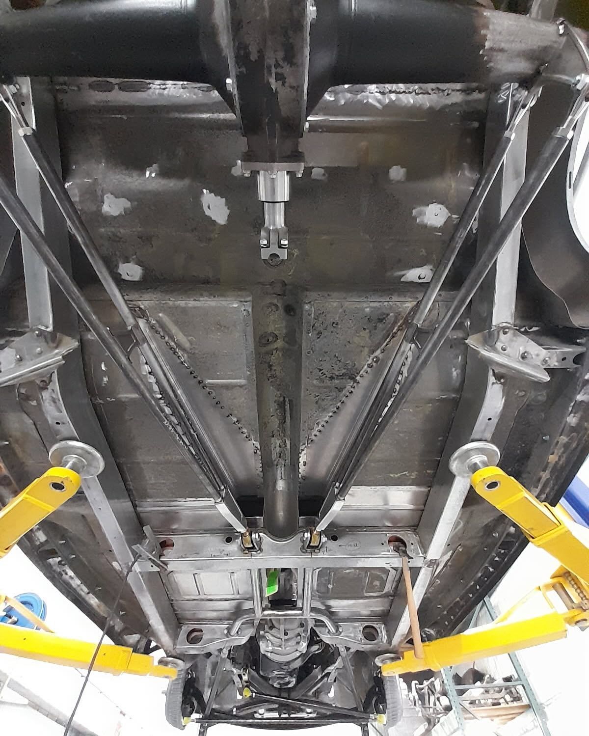 Undercarriage of a race car with exposed suspension and yellow control arms on a lift