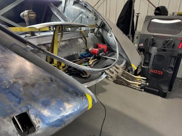 Damaged car in a garage with exposed frame and tools beside it