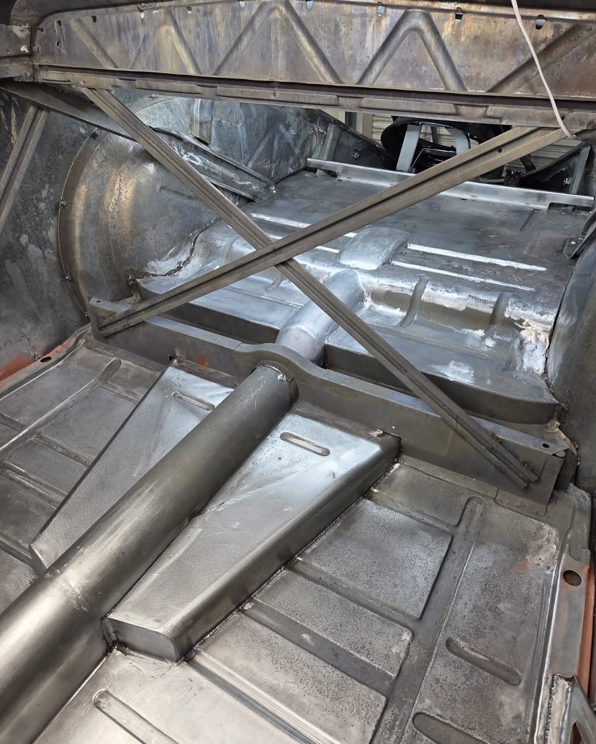 Metal car chassis interior with silver crossbars and ribbed floor panels under a roll cage