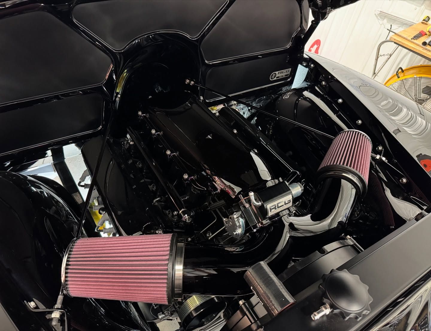 Close-up of a car engine bay with pink cone air filters and glossy black components.