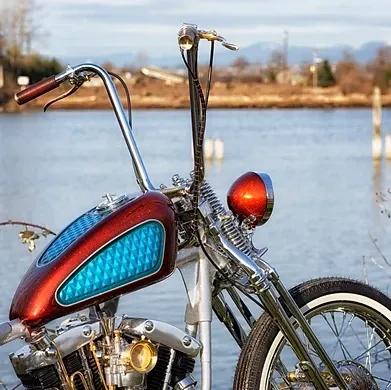 Custom red-and-blue motorcycle by the water with tall handlebars and a chrome headlight