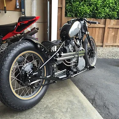 Custom black-and-white vintage motorcycle parked in a driveway beside a wooden fence