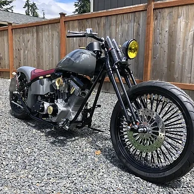 Custom black chopper motorcycle with yellow headlight on gravel beside a wooden fence.