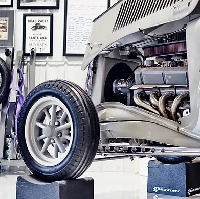 Custom vintage car on a lift, showing front wheel and exposed engine in a bright workshop.