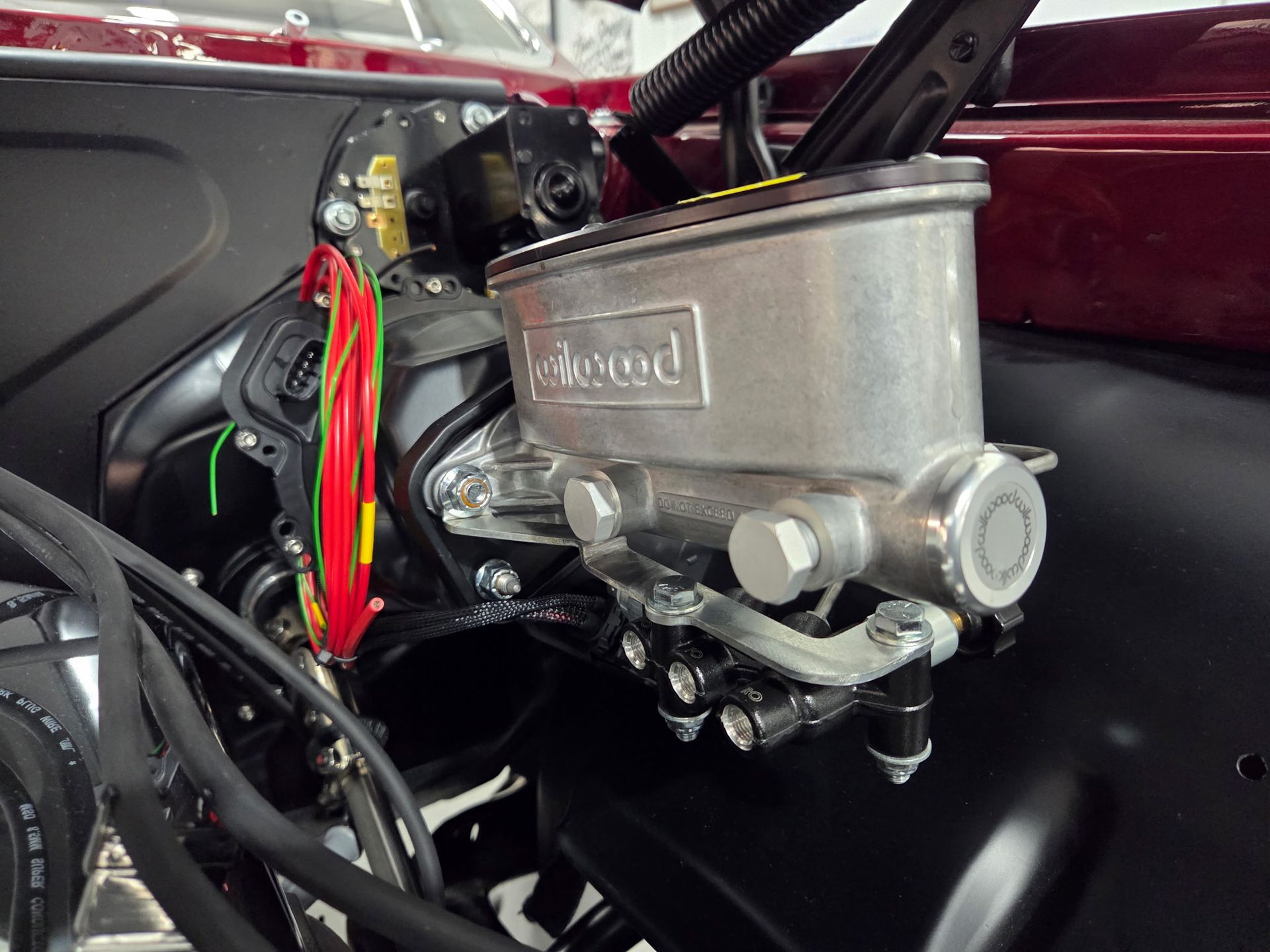 Close-up of a chrome carburetor with red and green wiring inside a car engine bay