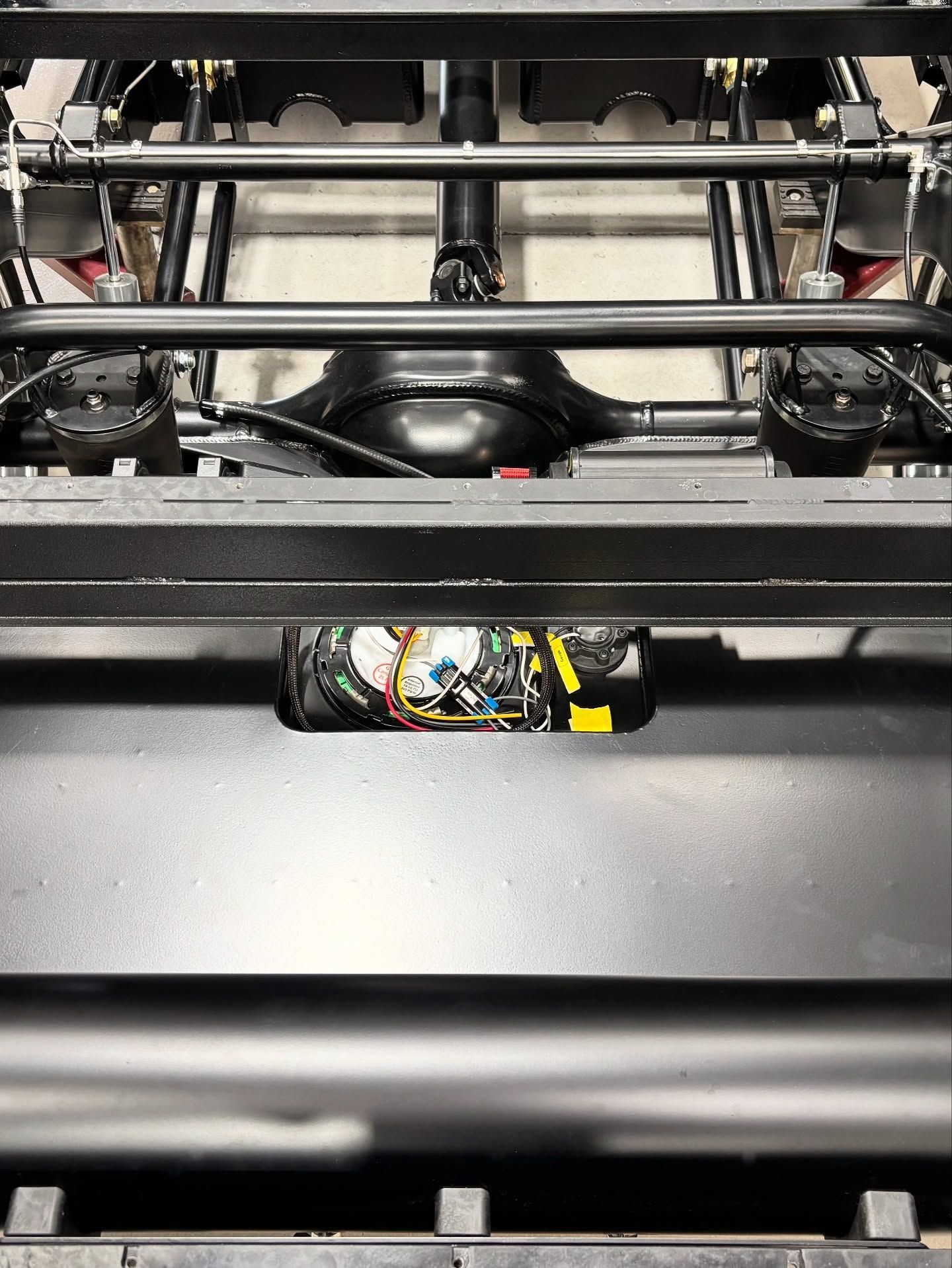 Close-up of a black mechanical assembly with wires and metal rods inside a machine frame