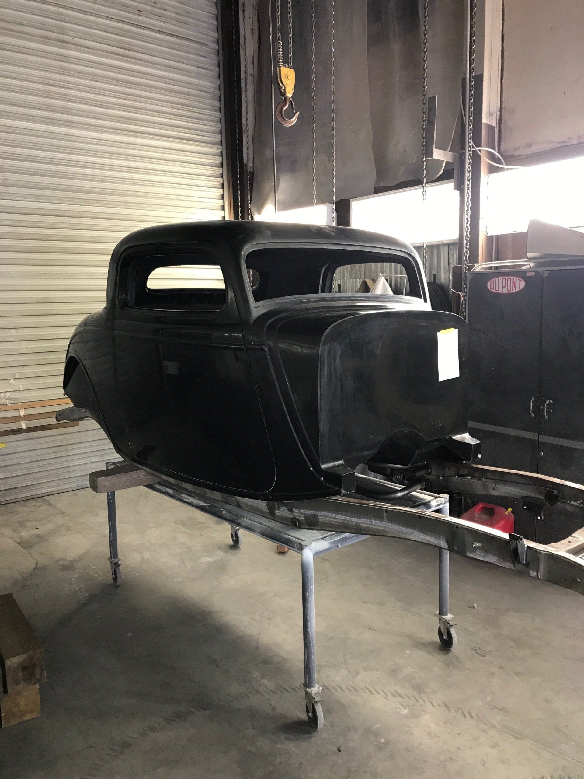 Black vintage car body on a metal stand in a workshop, unfinished and unpainted.