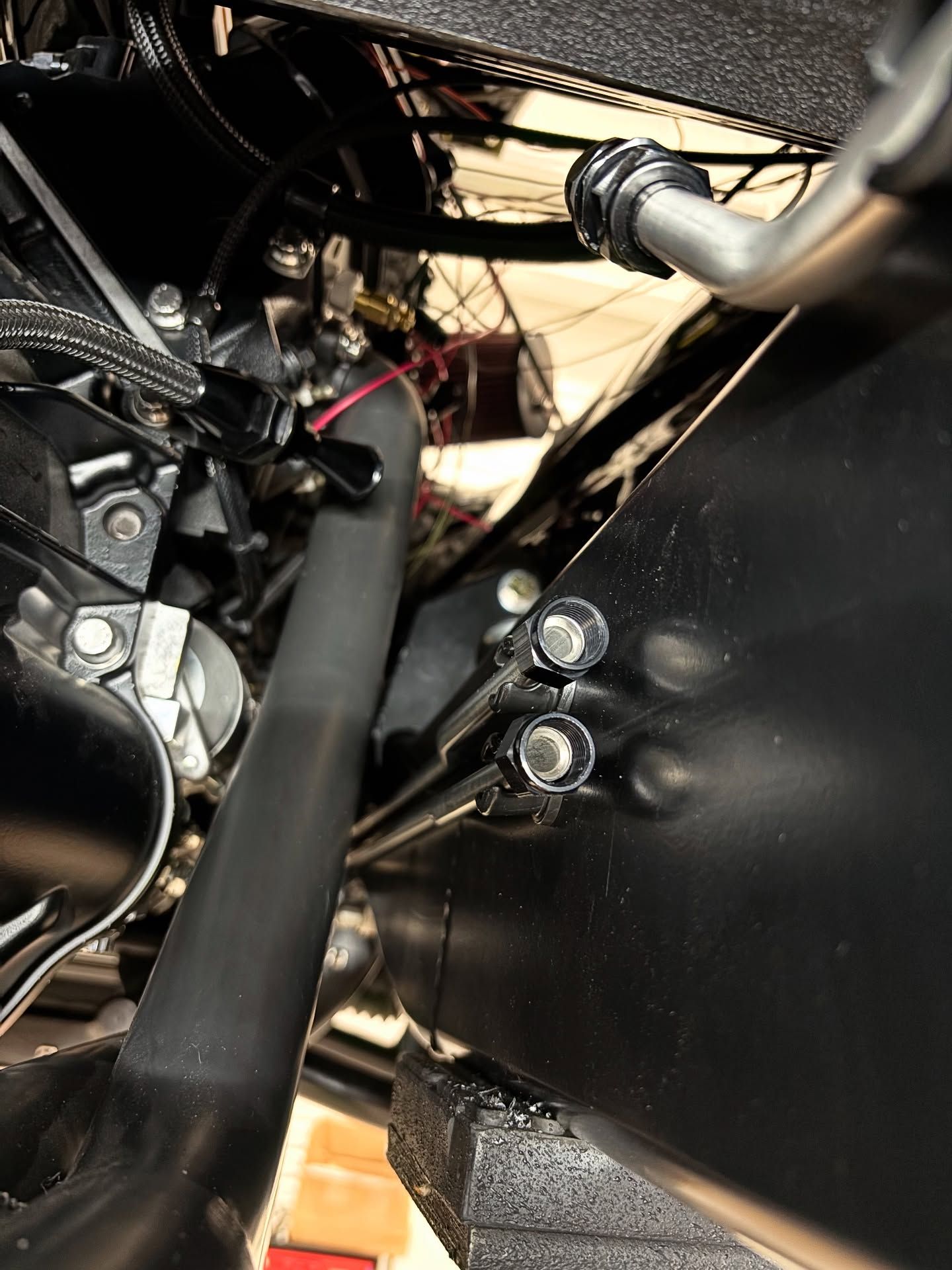 Close-up of black metal machinery with bolts, wiring, and a hose inside a tight compartment