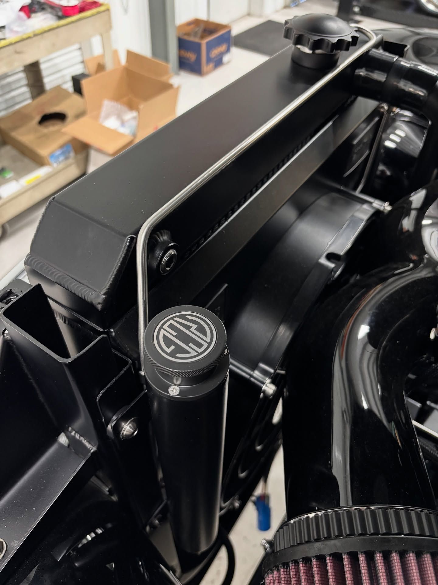Close-up of a black car engine bay with a round cap and metal frame in a garage.