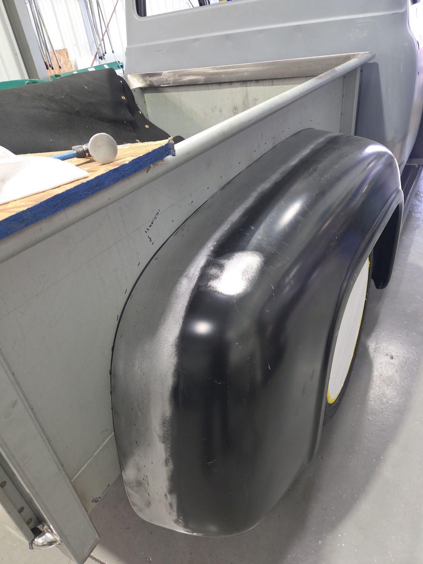 Black car fender leaning against a gray wall in a workshop or garage