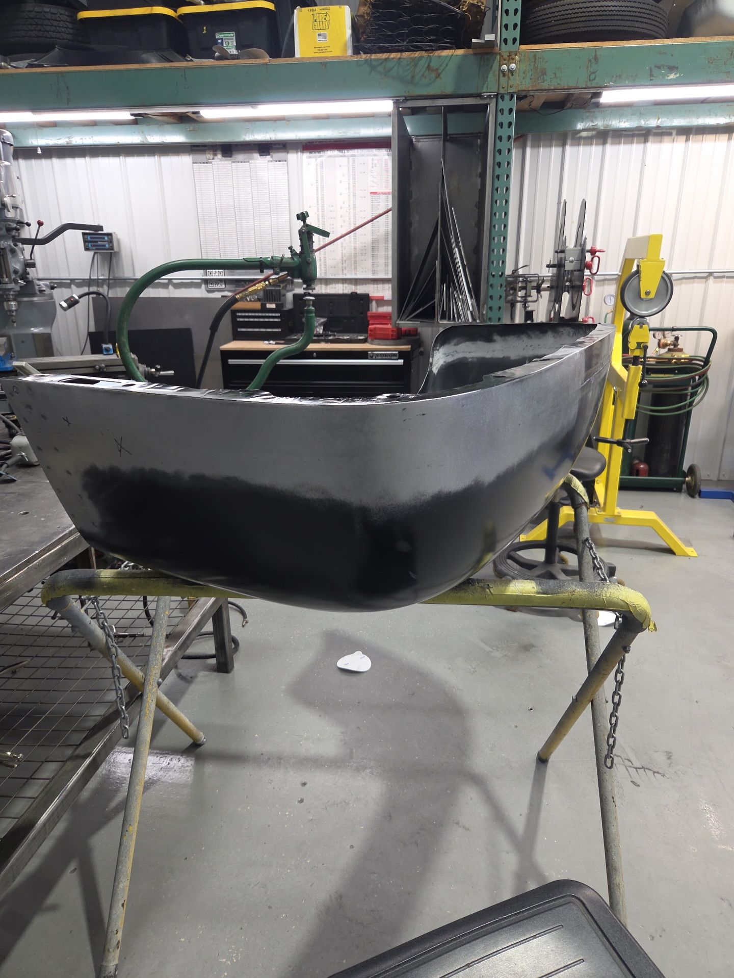 Black boat hull on metal supports in a workshop, with tools and equipment around it.