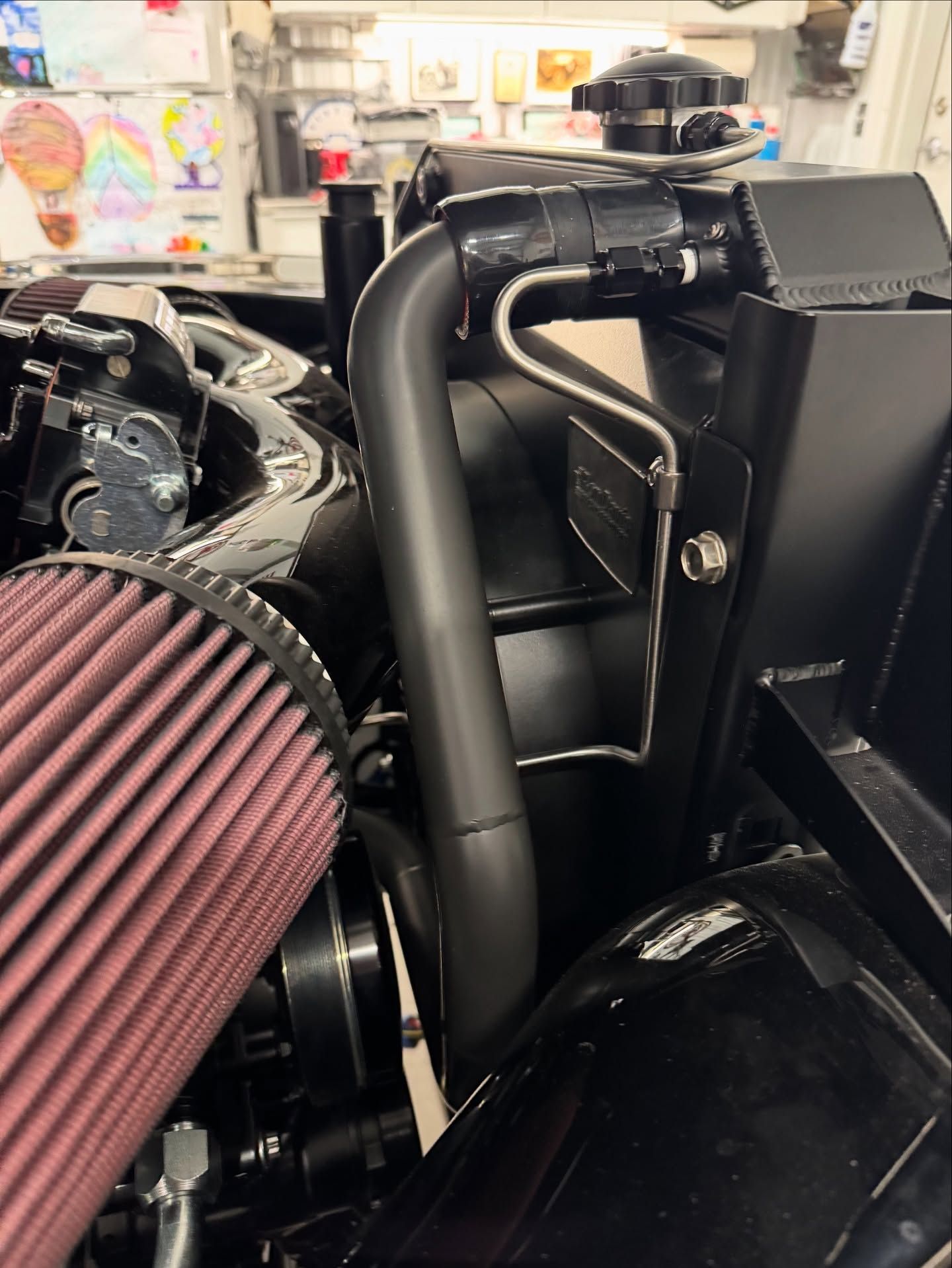 Close-up of a car engine bay with a red air filter and black intake pipes in a workshop
