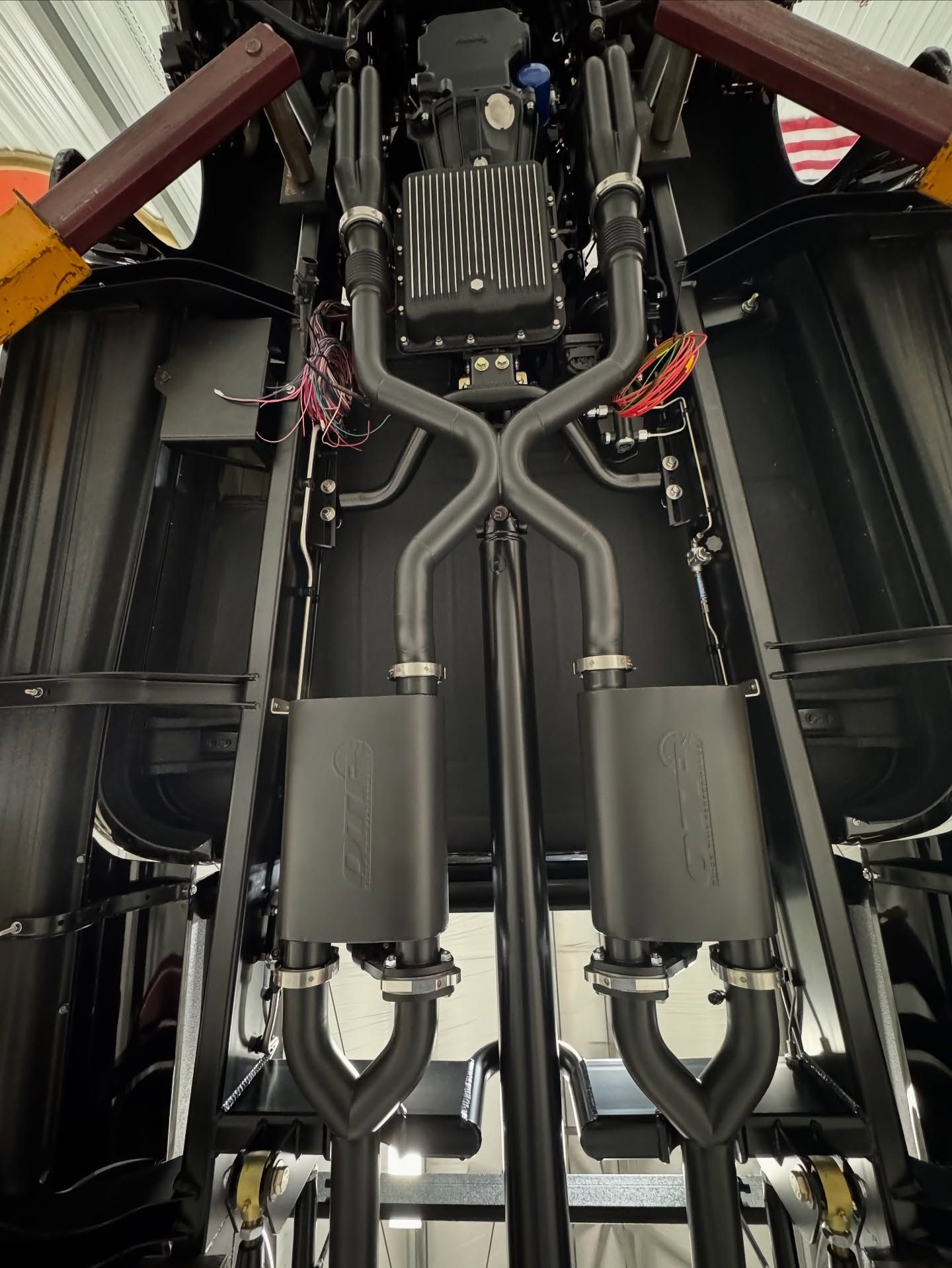 Close-up of industrial machinery with black hoses, metal pipes, and red cable ties inside a compartment