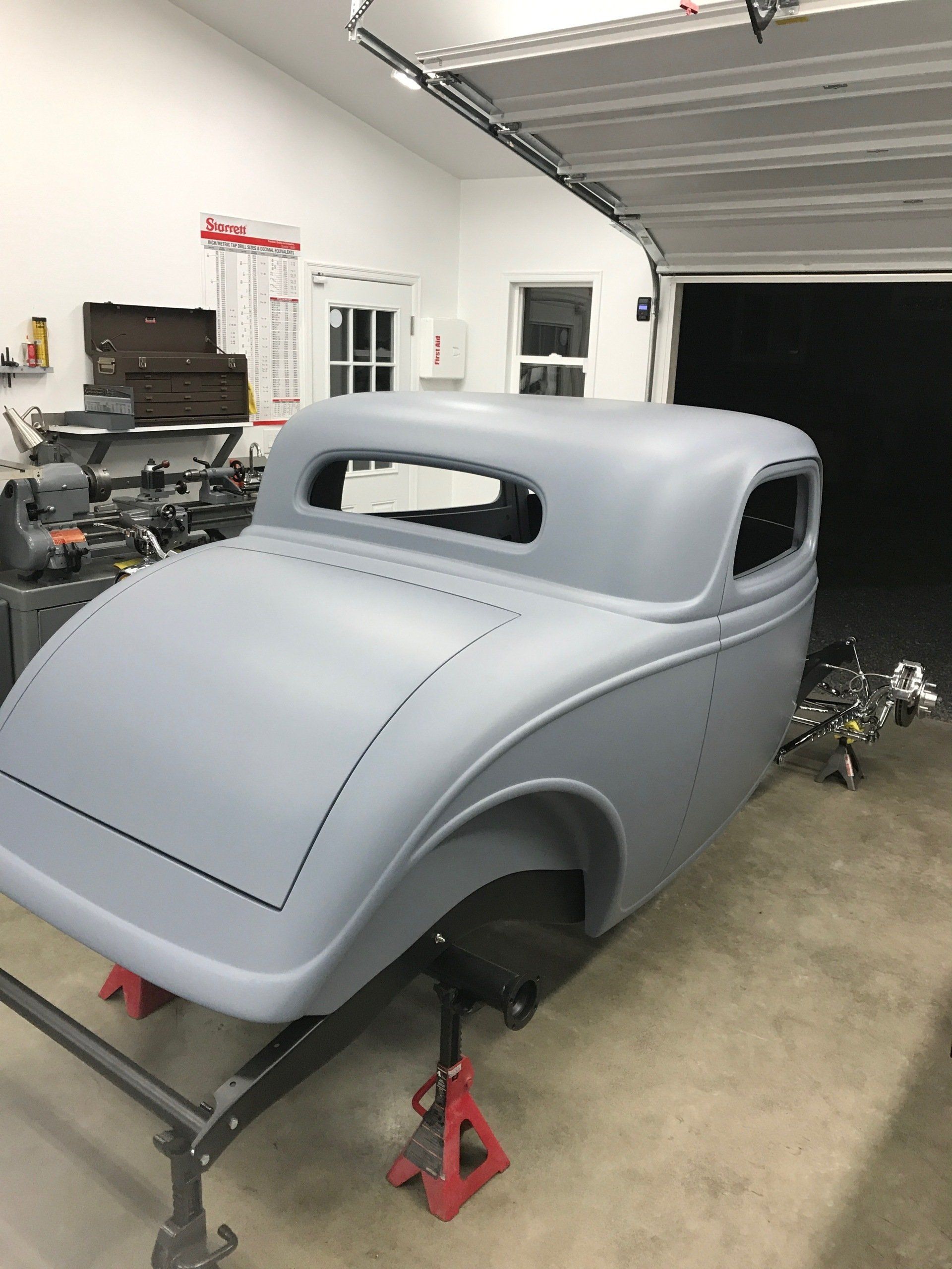 Gray custom car body shell on a frame inside an auto shop garage.