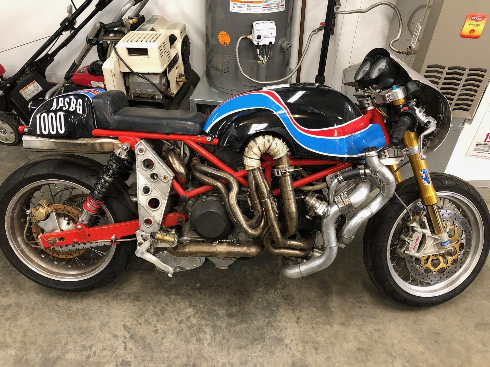 Custom blue-and-red motorcycle with exposed engine and chrome exhaust, parked indoors against a wall.