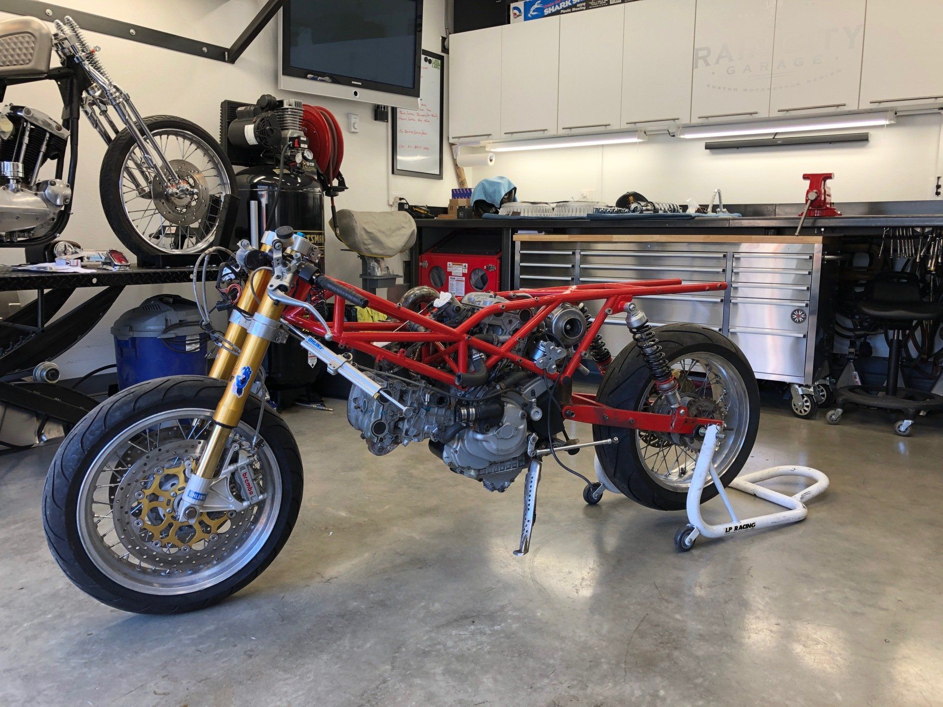 Red minibike frame on a rear stand in a garage, with tools and bike parts in the background