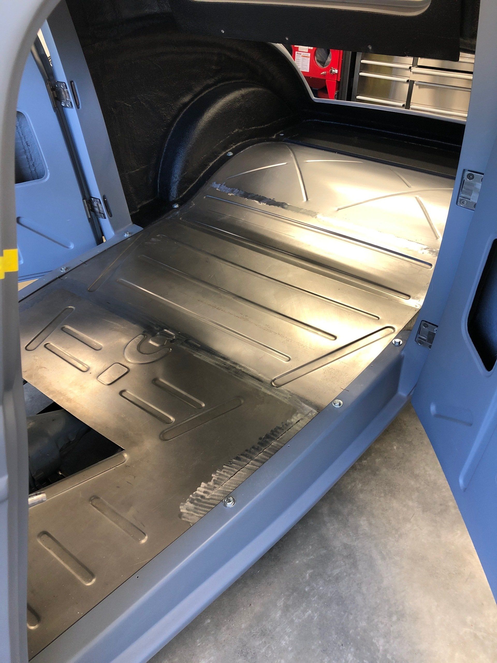Shiny black rear cargo floor of a vehicle, viewed through an open side door.