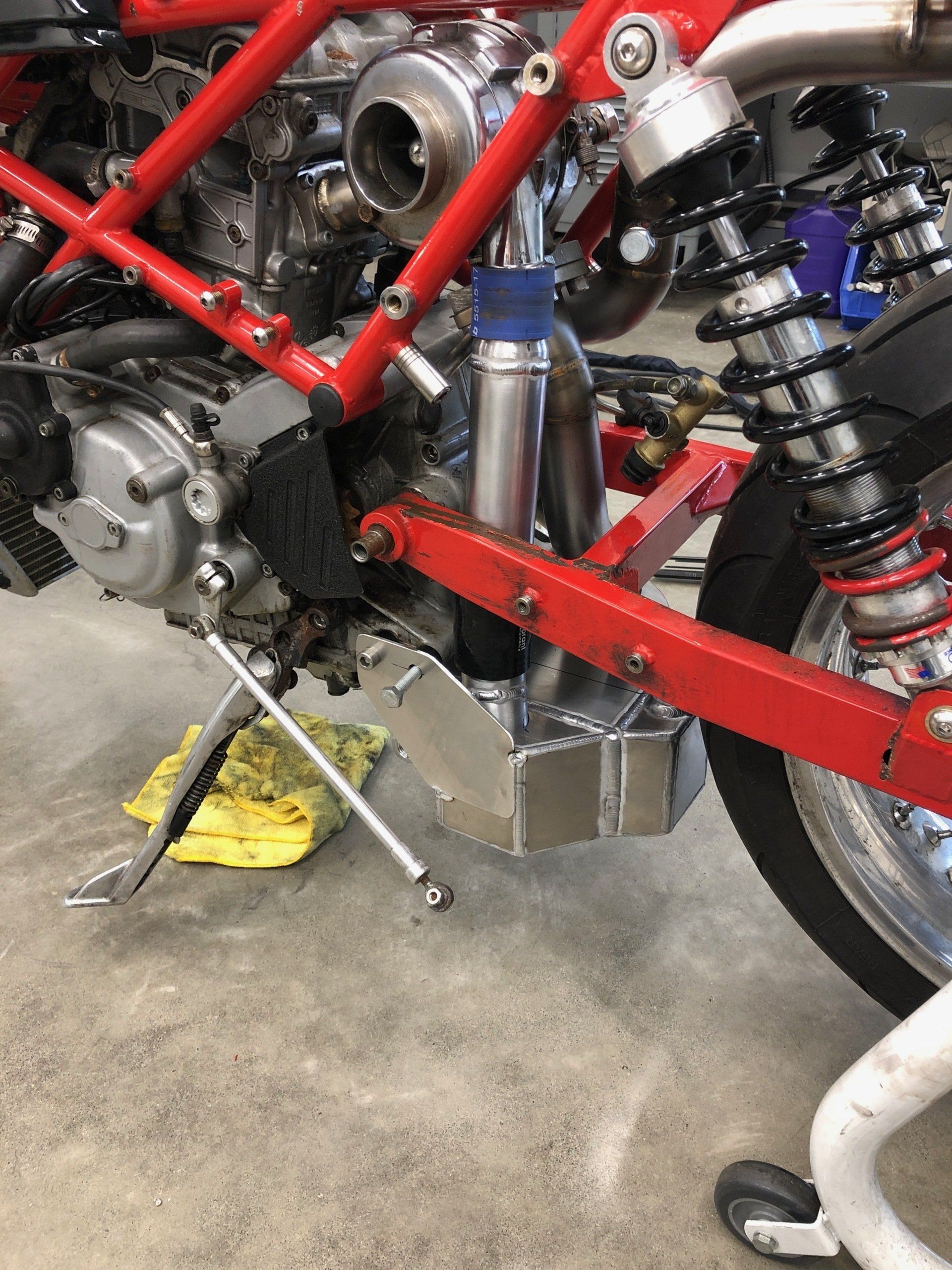 Custom motorcycle frame and engine in a workshop, with red frame tubing and black suspension.