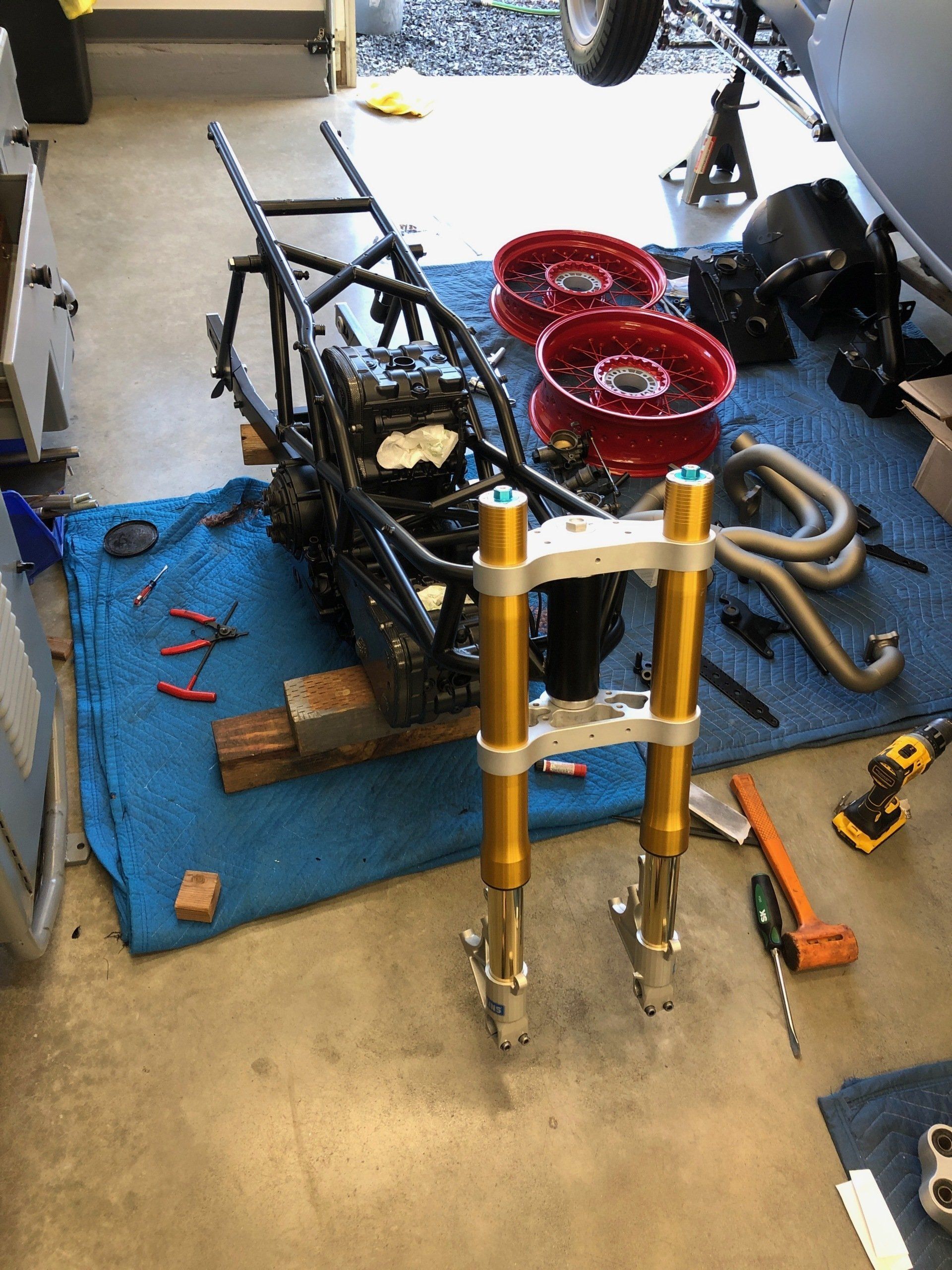 Motorcycle frame on a blue mat with gold forks and red wheels in a garage workshop