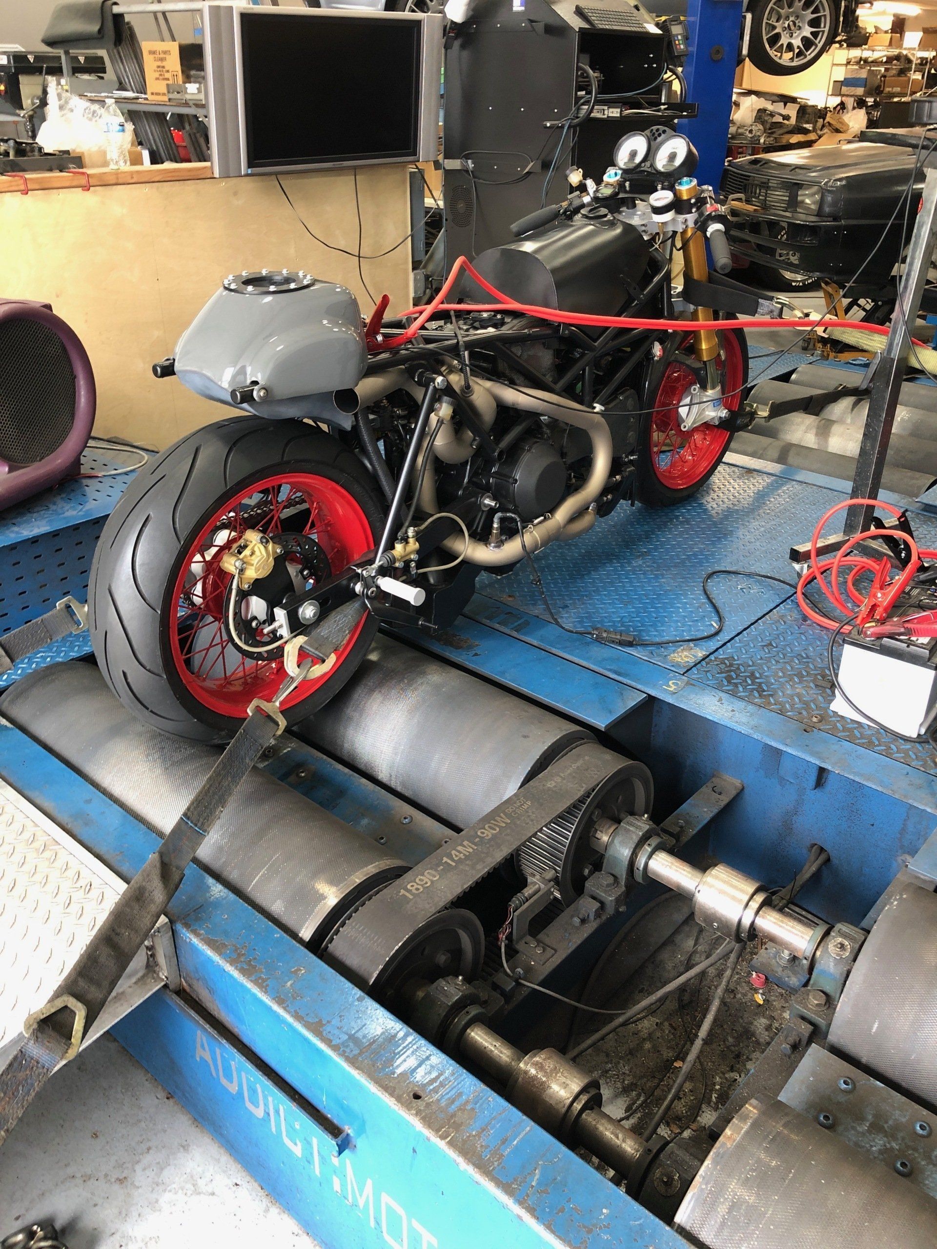 Red motorcycle on a blue dynamometer in a workshop, secured with straps.