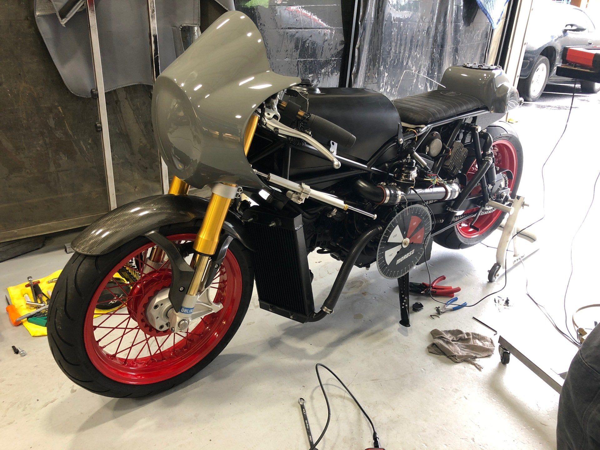 Custom black motorcycle with red wheels in a workshop, partially disassembled on a stand.