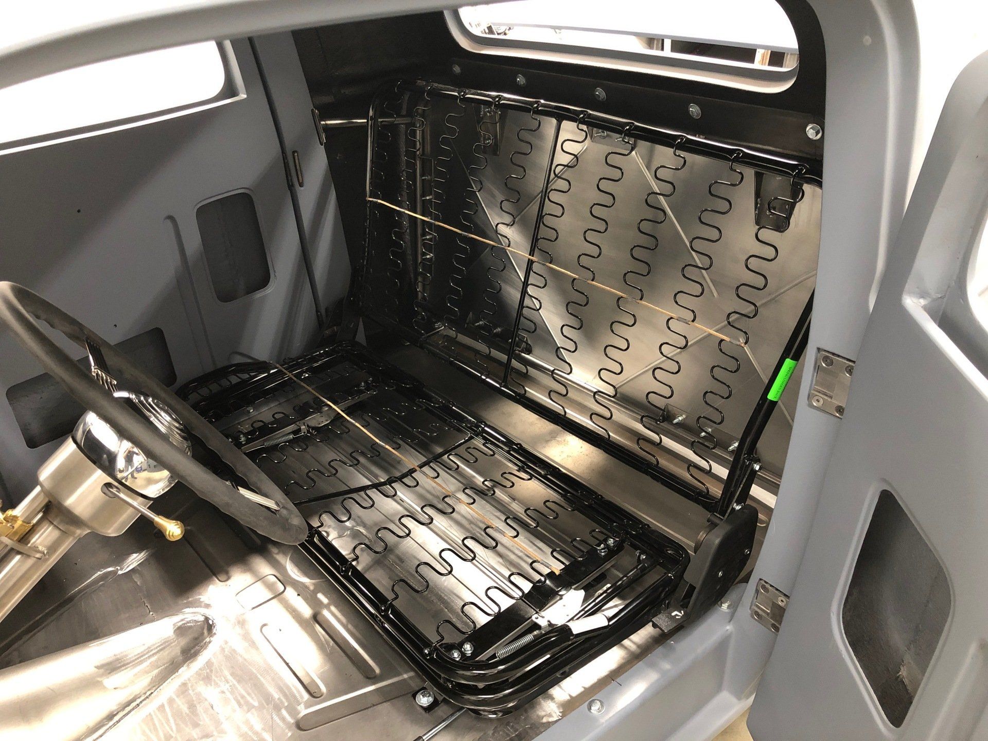 Gray car interior with a black leather seat, steering wheel, and visible sound-deadening panels on the floor and door.