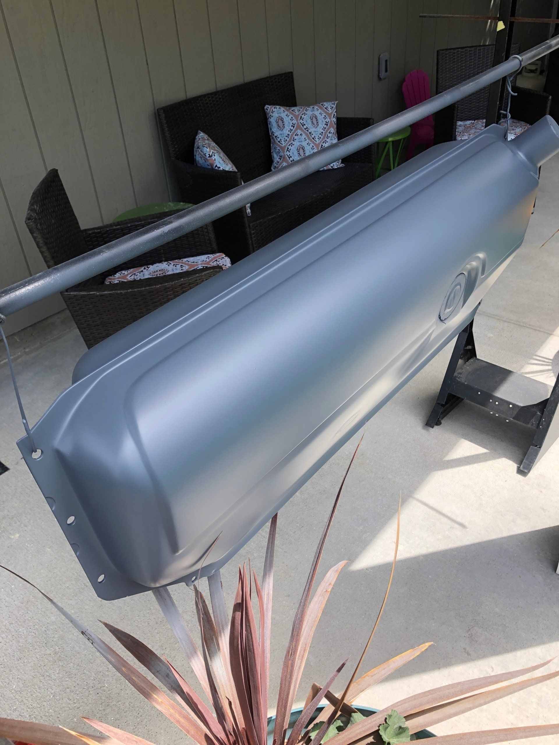 Gray metal mailbox on a porch railing beside outdoor chairs and a potted plant.