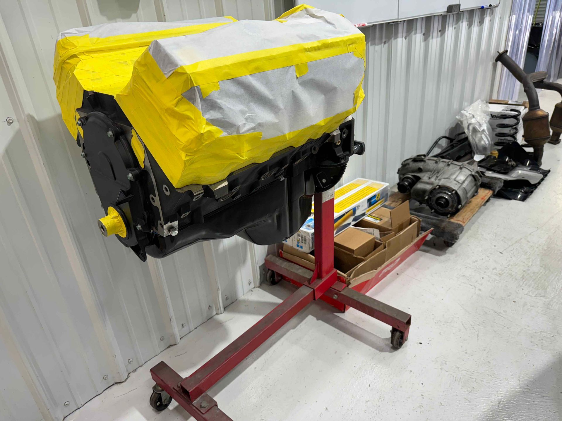 Engine on a red stand, partially covered with yellow tape, in a workshop with parts nearby