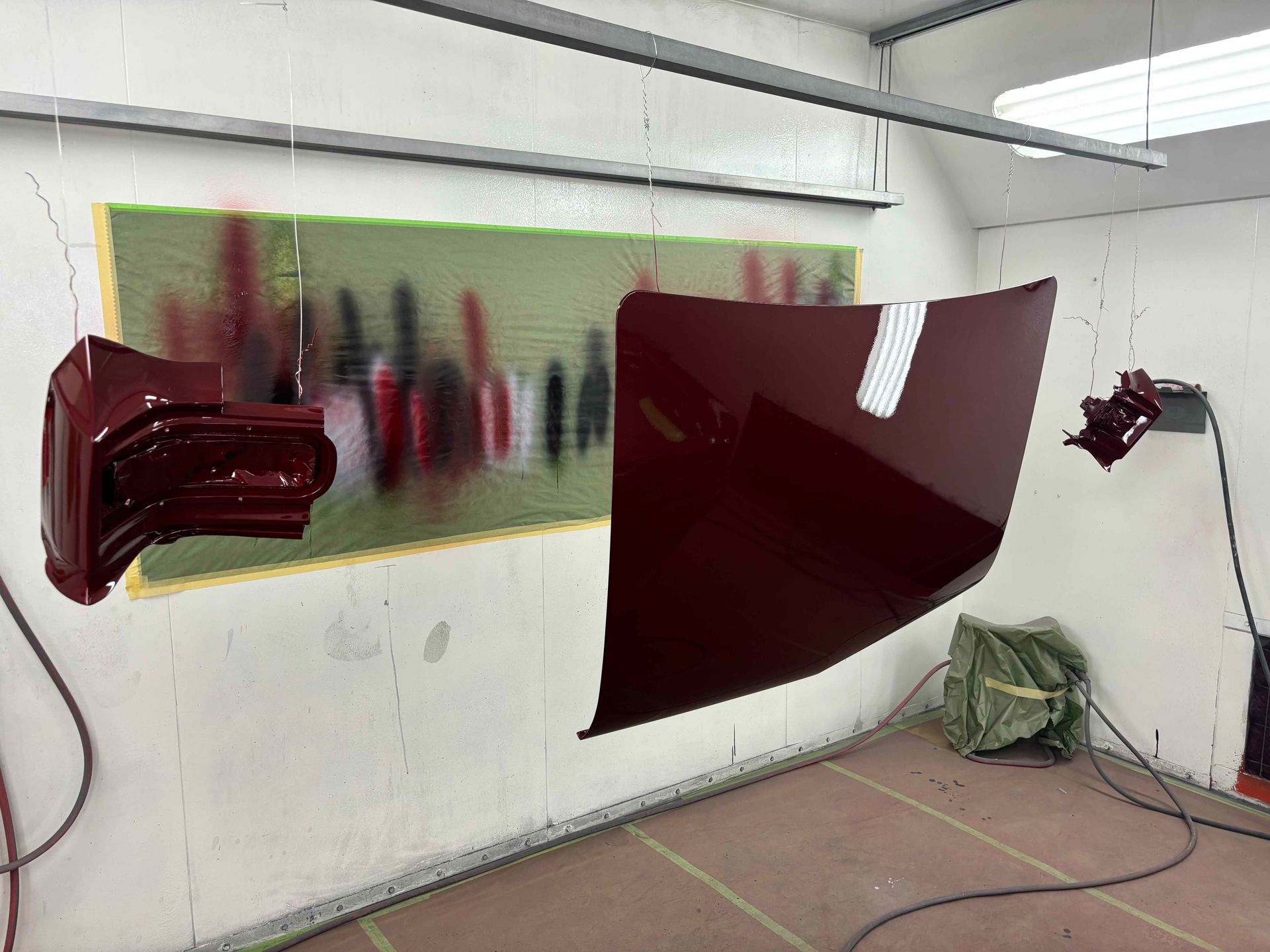 Abstract maroon paint-like shapes on a wall in a white room with a hazy green-red panel and floor cords