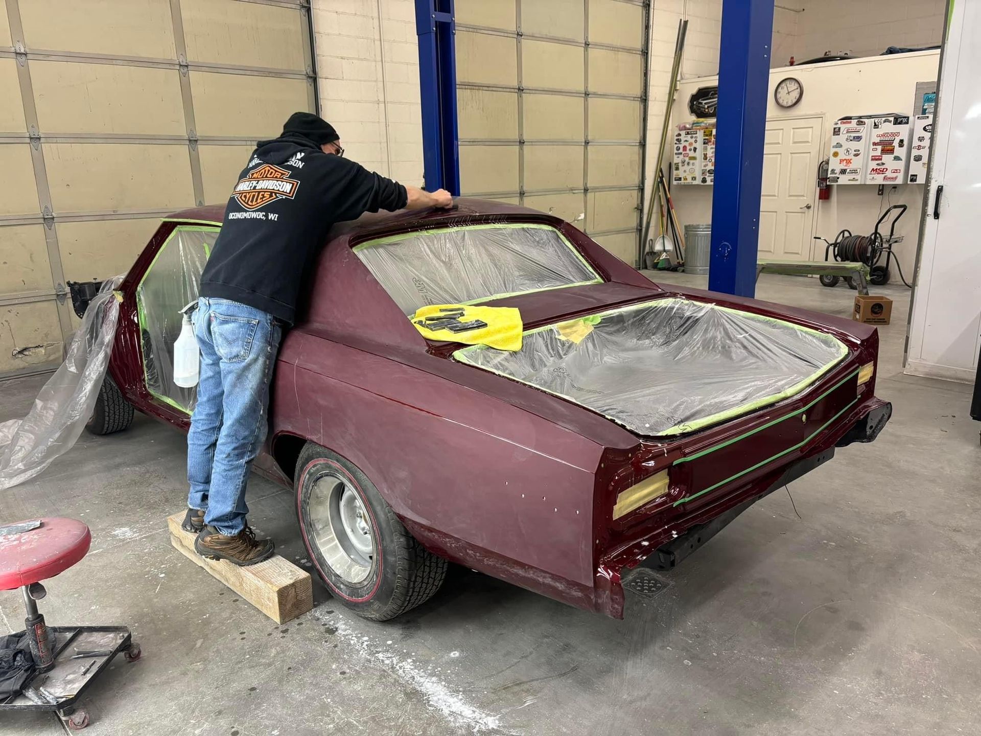 Person sanding a maroon car body in a garage workshop