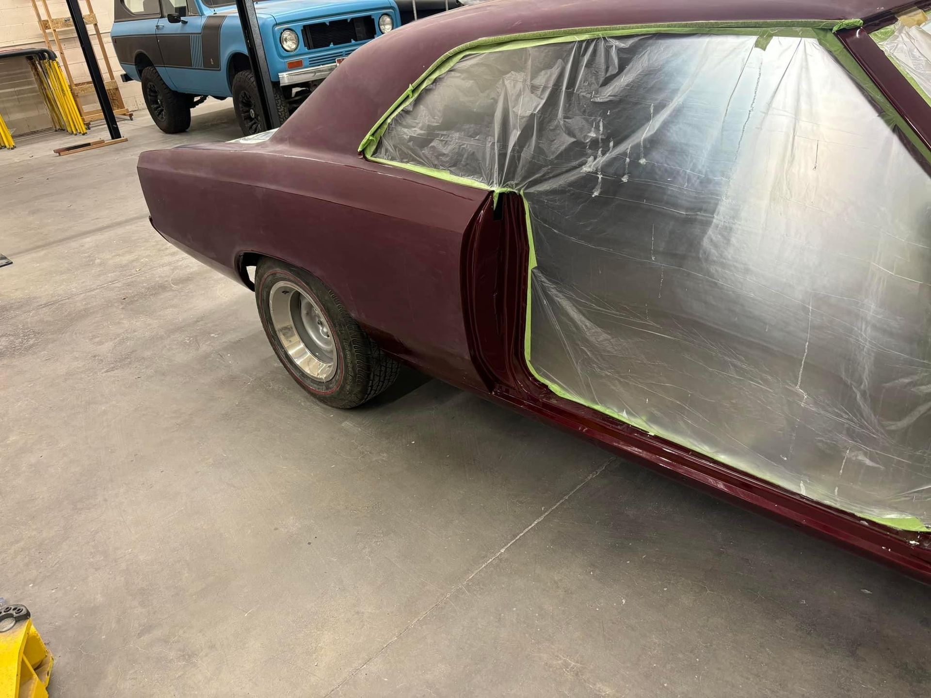 Maroon car with plastic-covered windows in a workshop or paint area