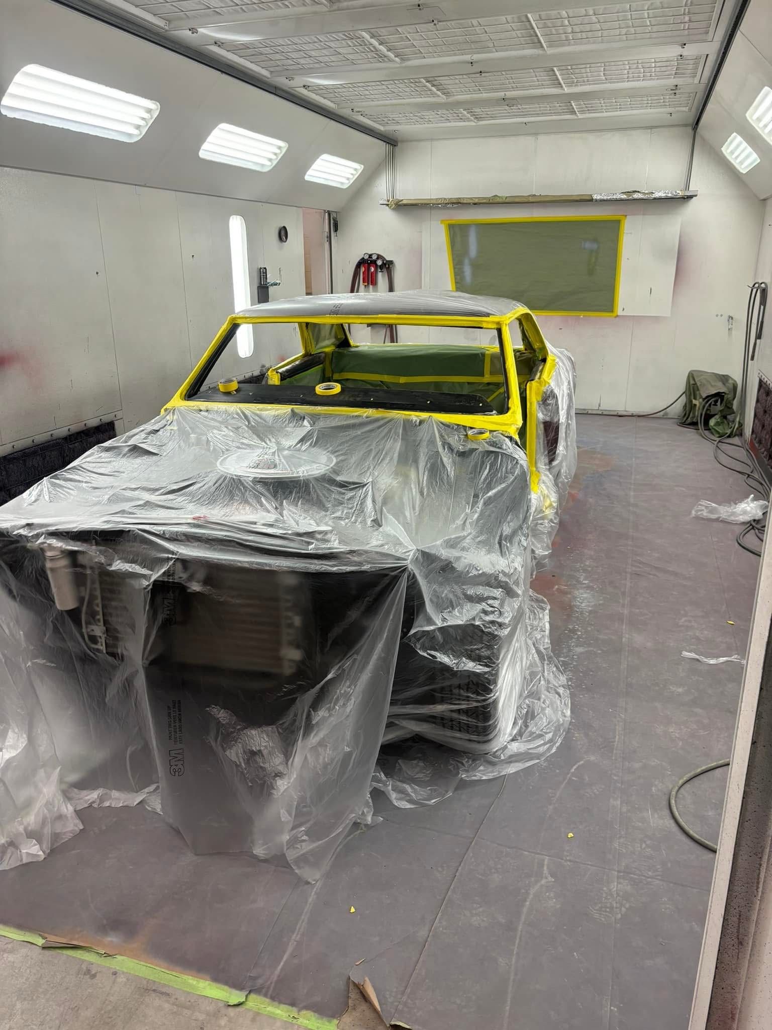 Masked car body in a spray booth, covered in plastic and yellow tape for painting
